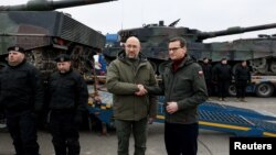 Thủ tướng Ukraine Denys Shmyhal và Thủ tướng Ba Lan Mateusz Morawiecki bắt tay bên cạnh những chiếc xe tăng Leopard 2 đầu tiên được giao từ Ba Lan vào ngày kỉ niệm một năm Nga xâm lược Ukraine, tại một địa điểm không được tiết lộ, Ukraine, ngày 24 tháng 2 năm 2023. 