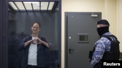 Wall Street Journal reporter Evan Gershkovich, who is in custody on espionage charges, makes a heart-shaped gesture inside an enclosure for defendants before a court hearing in Moscow, April 23, 2024.